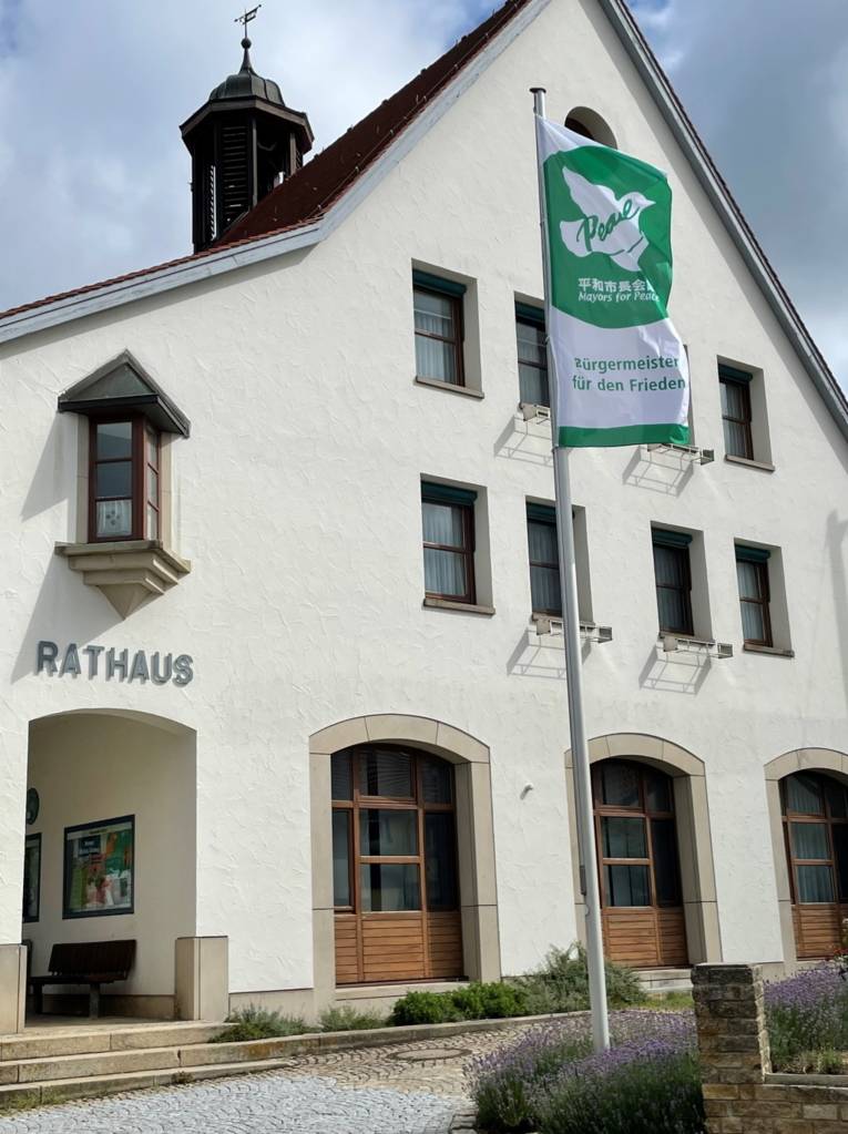Die grün-weiße Mayors-for-Peace-Flagge weht vor dem Rathaus in Hülben im Wind.